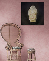 Wicker chair and wooden stool against a pink wall with a Buddha head painting.