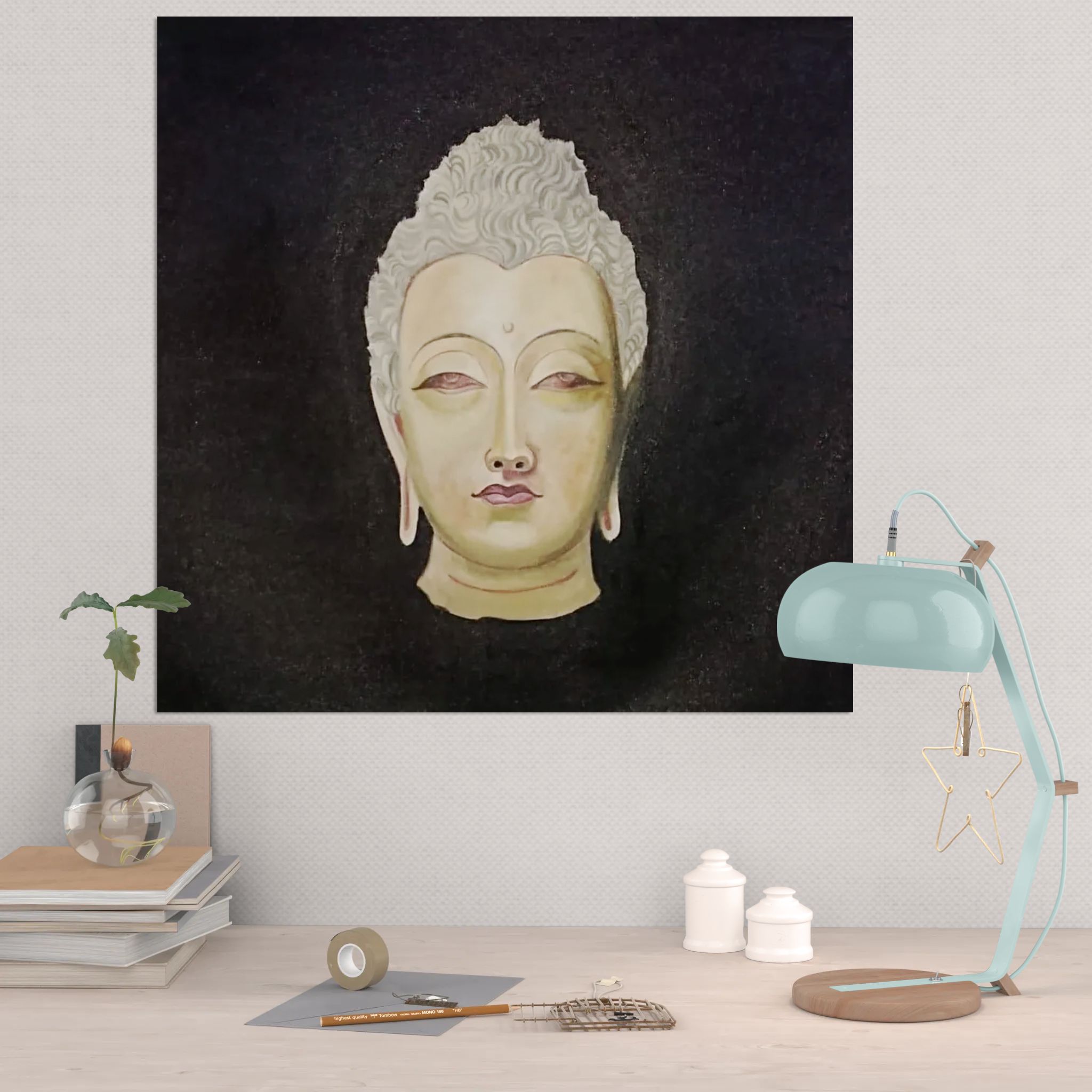 Framed artwork of a Buddha head on a wall above a desk with a lamp and books.